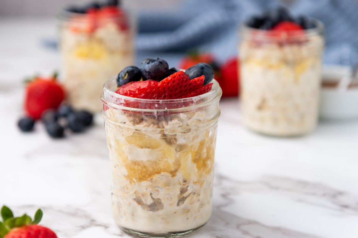 Three pint mason jars filled with overnight oats and topped with strawberries and blueberries.