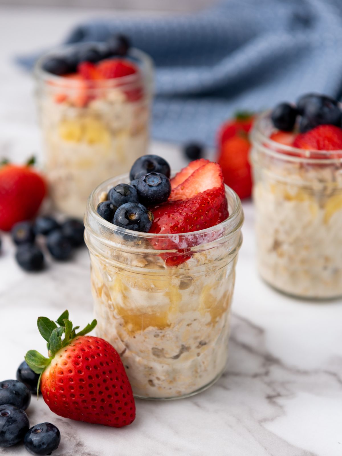 Three pint mason jars filled with overnight oats and topped with strawberries and blueberries.